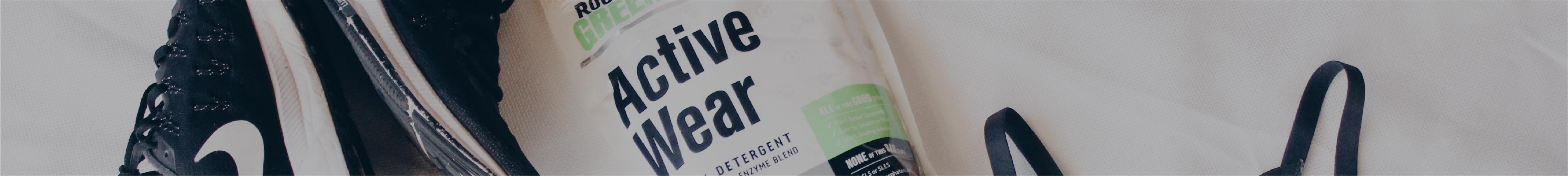 Close-up of a bottle labeled Active Wear next to black athletic shoes and a black strap on a white surface.