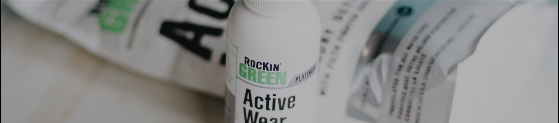 Close-up of a white bottle labeled Rockin Green Active Wear with blurred packaging in the background.