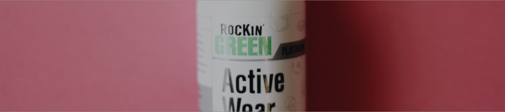 Close-up of a bottle labeled Rockin Green Active Wear against a pink background.