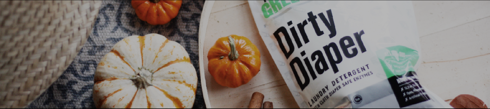Small pumpkins and a pack of Dirty Diaper laundry detergent on a patterned cloth and wooden surface.