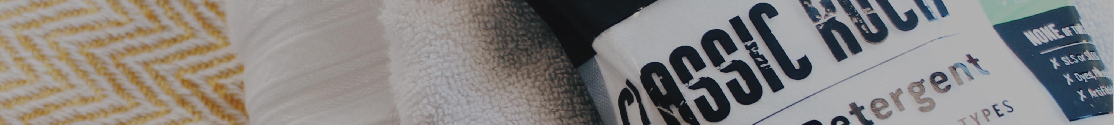 A bottle of laundry detergent near folded towels, one yellow-striped and one white.