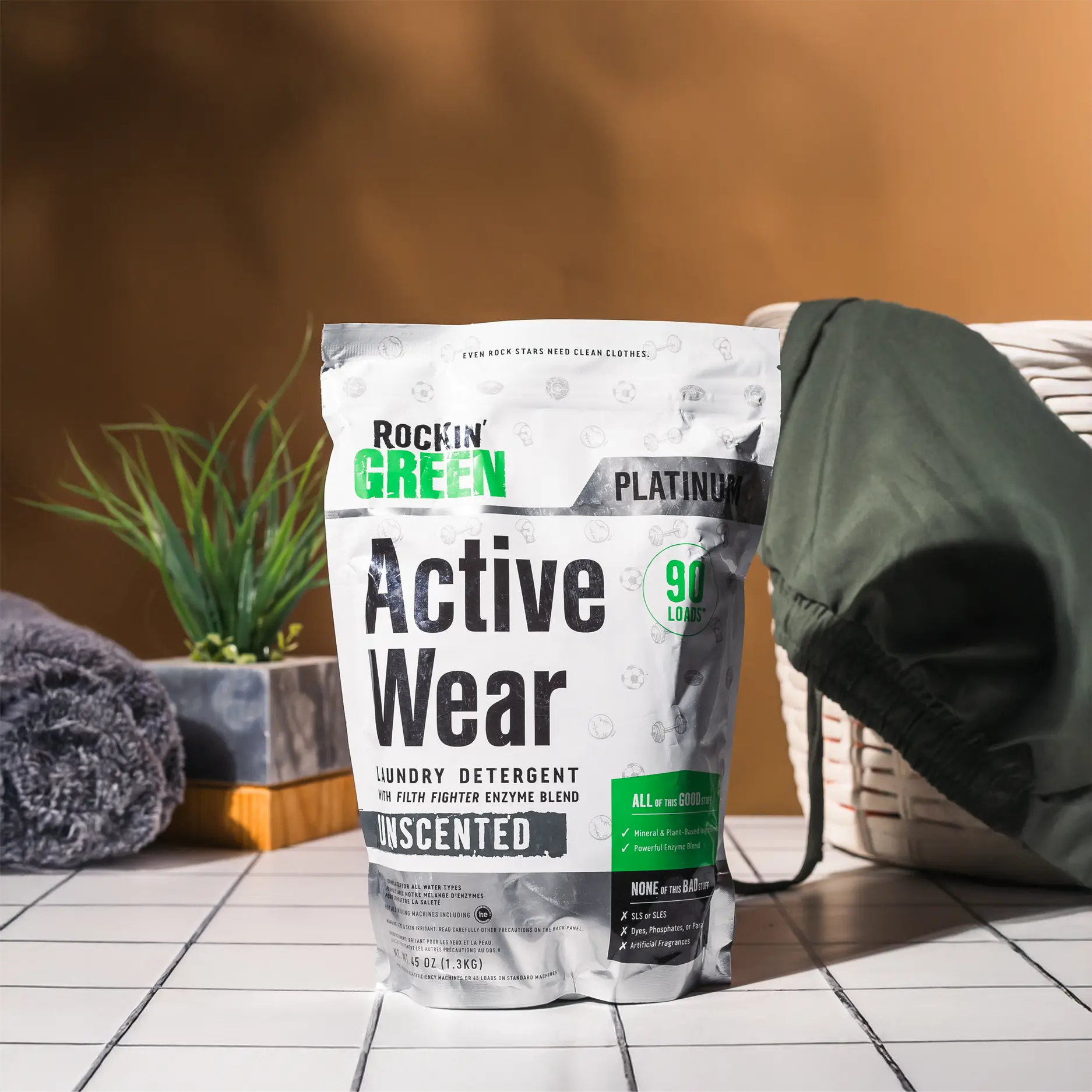 Close-up of a bottle labeled Active Wear next to black athletic shoes and a black strap on a white surface.