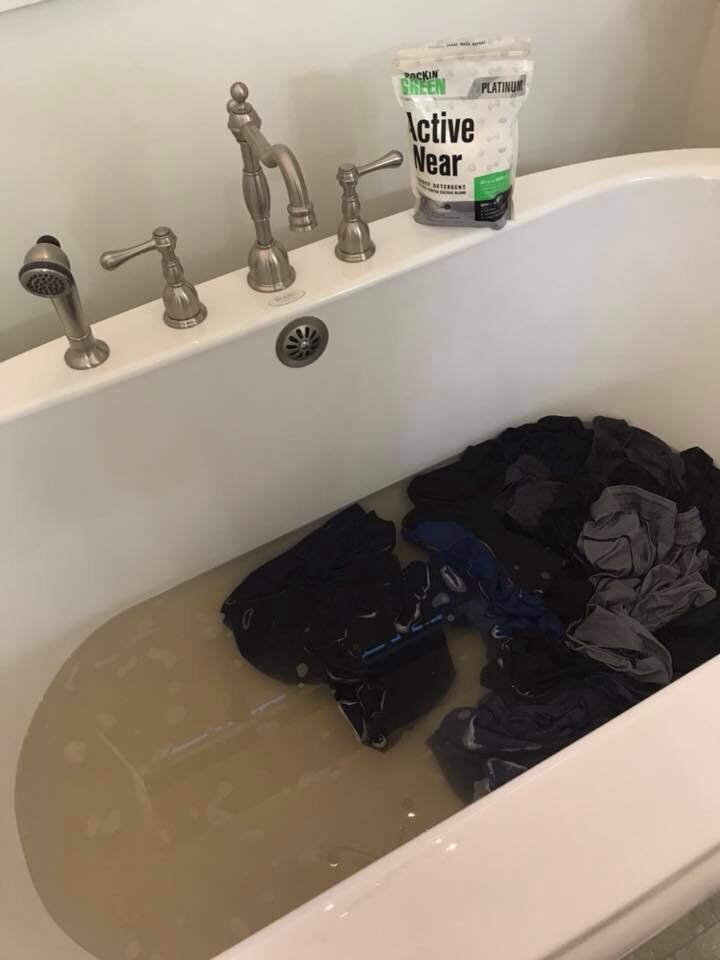 Clothes soaking in a bathtub with murky water and detergent on the tub edge.