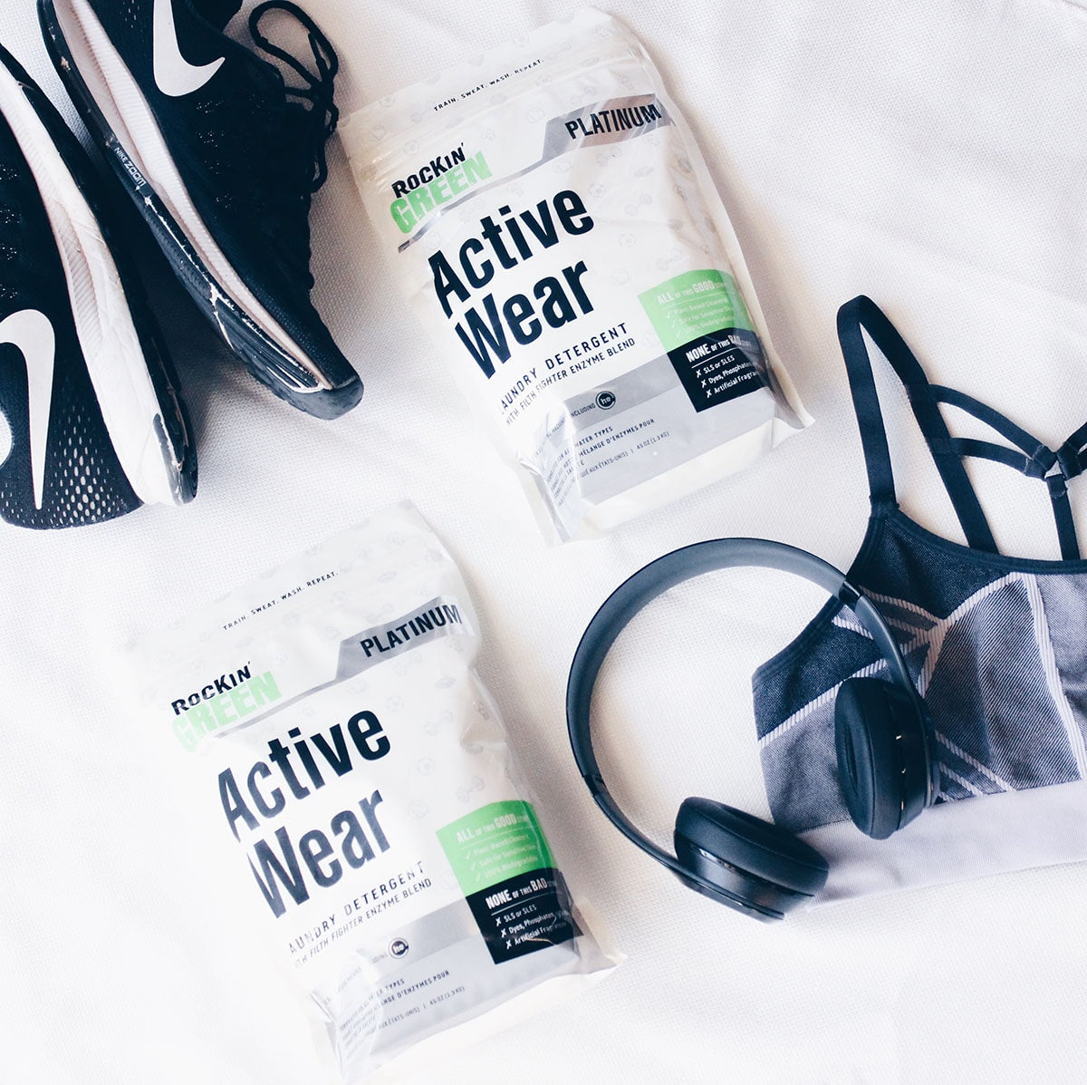 Workout gear with sneakers, headphones, sports bra, and Rockin Green Active Wear detergent two packs.