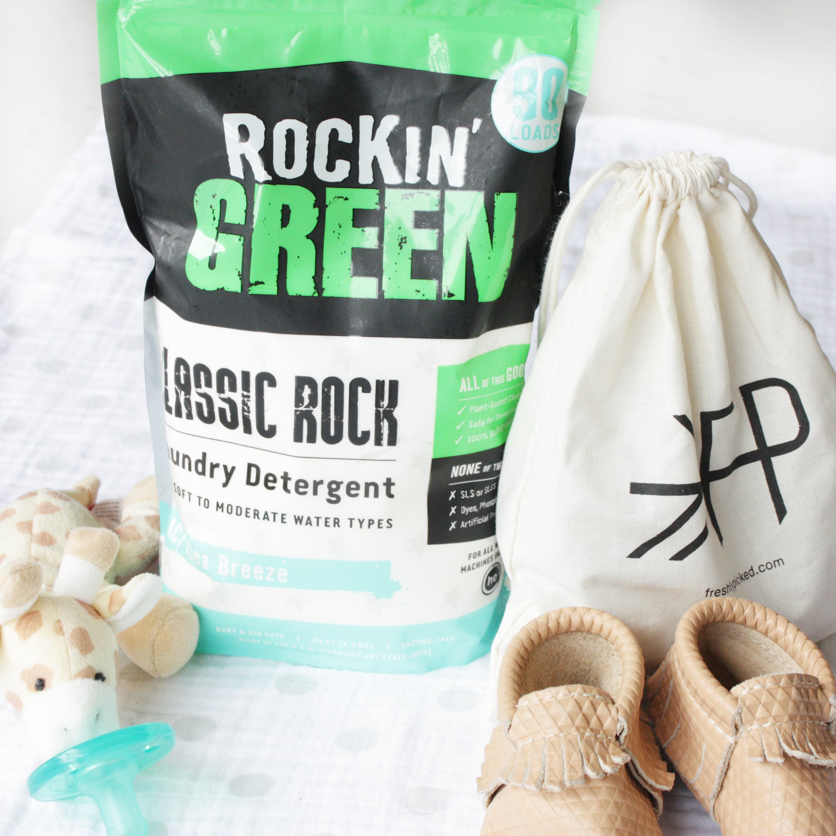 Classic Rock Laundry Detergent - AC/DSea Breeze, baby shoes, pacifier, plush toy, and drawstring bag on white.