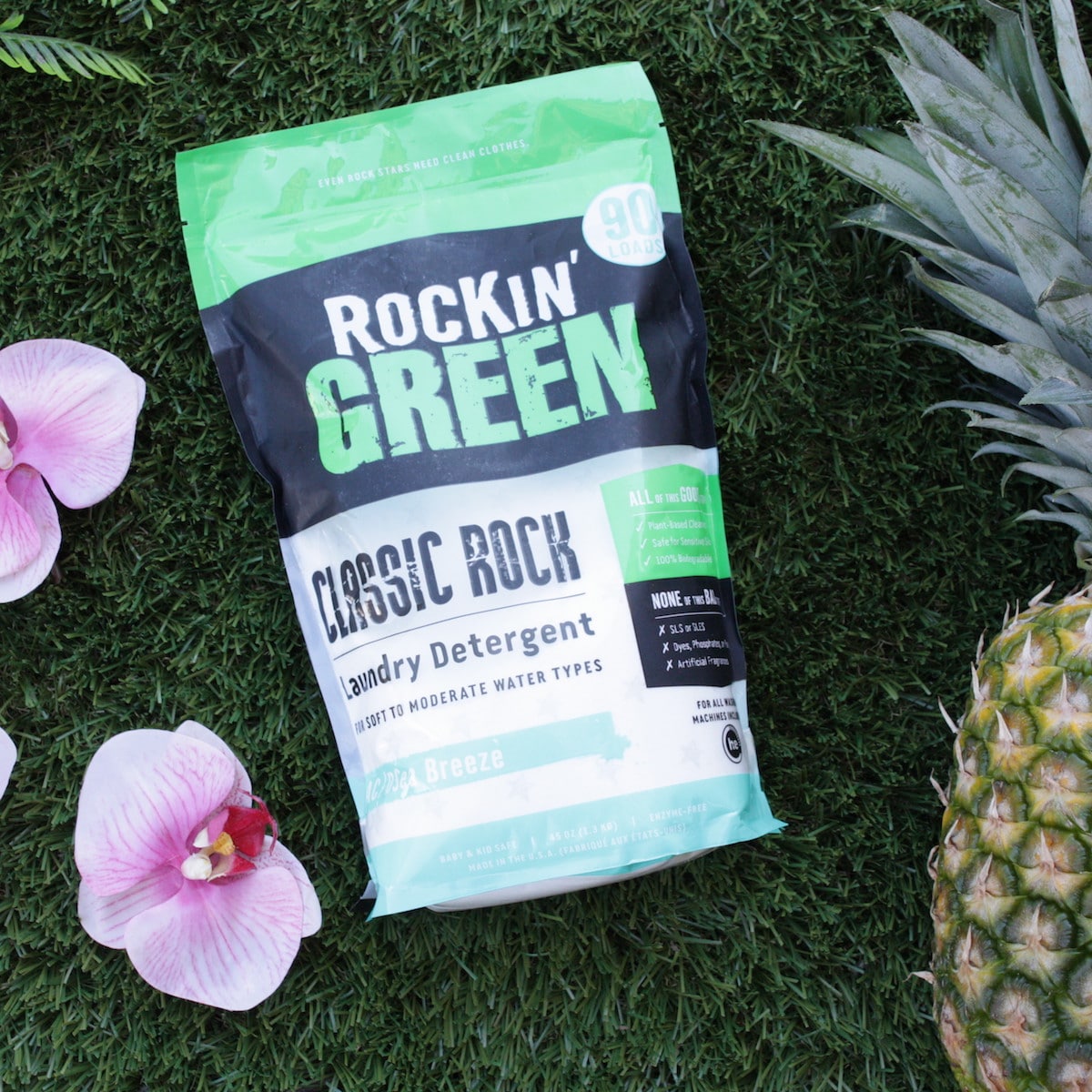 AC/DSea Breeze detergent on grass, orchids around and a pineapple nearby. Brand: Rockin Green.
